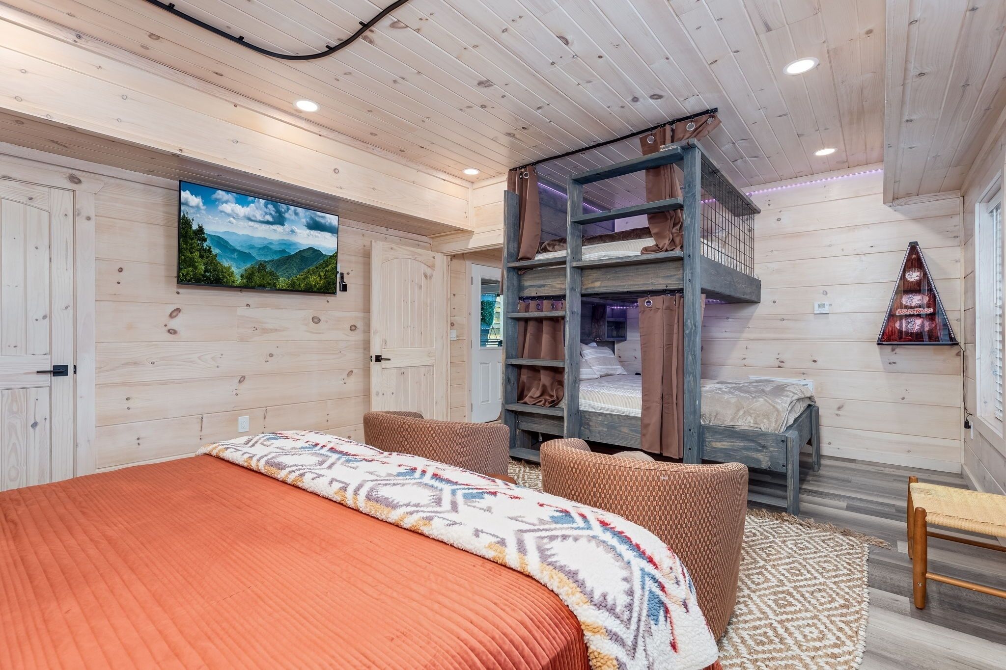 A cozy room with a bed, a bunk bed, a TV, and a wooden ceiling.
