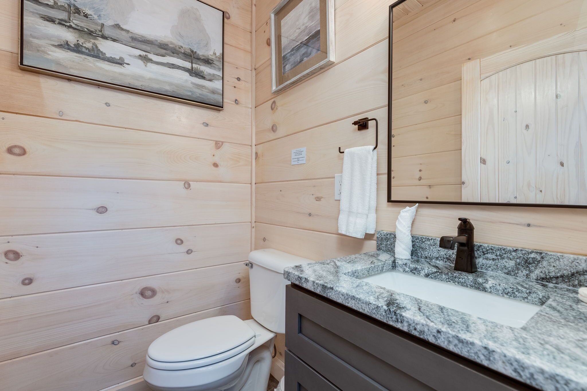 A wooden-paneled bathroom with a toilet, sink, and mirror.