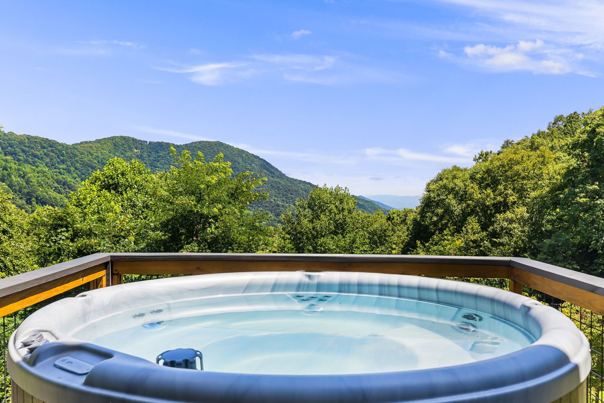 Een hottub op een houten terras met uitzicht op een bebost berglandschap.