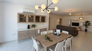 Una cocina moderna con comedor, sillas blancas, una mesa de madera y un televisor integrado.