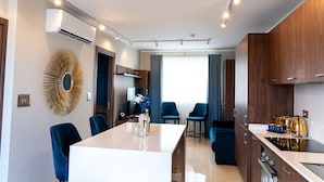 A modern hotel room with a central island dining table, two blue armchairs, a TV, and a minibar. - Domus Boutique Hotel (Rabat)