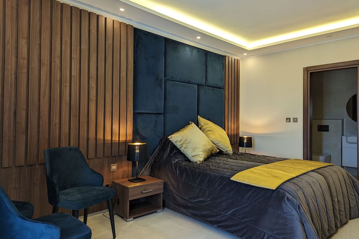 Un dormitorio moderno con una cama grande, dos mesitas de noche, una silla y un armario.