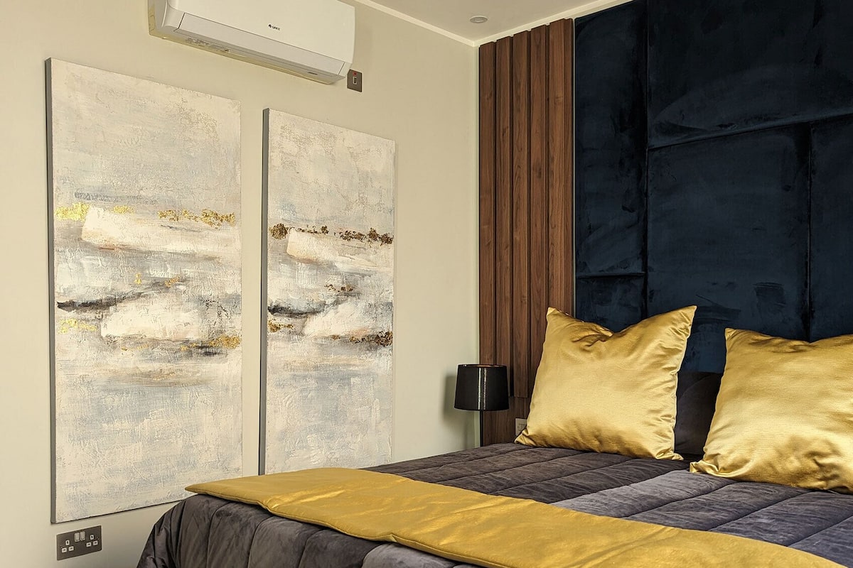 Un dormitorio moderno con una cama grande, cabecera de madera oscura y dos cuadros abstractos en la pared.