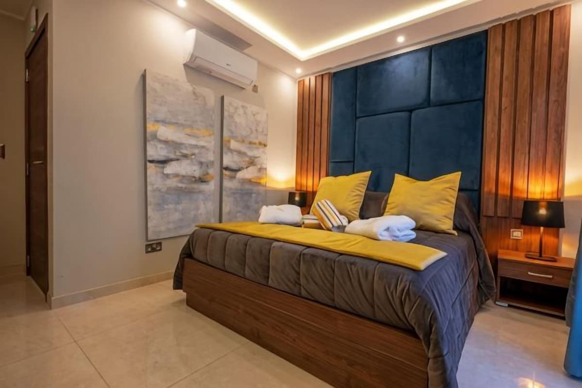 A modern bedroom with a large bed, bedside lamps, and a wall-mounted air conditioner.