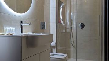 A modern bathroom with a glass-enclosed shower, a large oval mirror, and a white sink.
