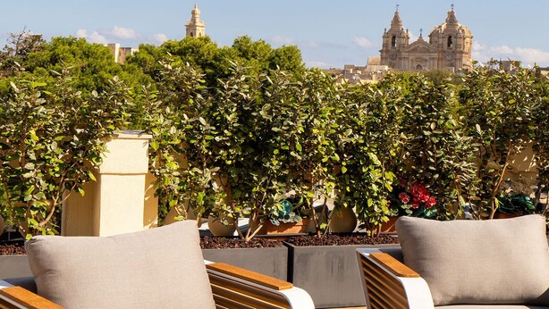 A rooftop terrace with two lounge chairs and a wooden table, overlooking a historic building with two towers. - Domus Boutique Hotel (Rabat)