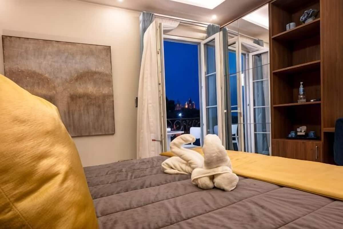 Un dormitorio con cama, sofá, estante de madera y vistas a través de un ventanal.