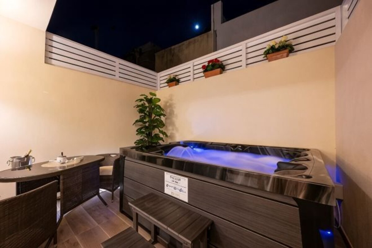 A hot tub with a bench, a small table, and potted plants.