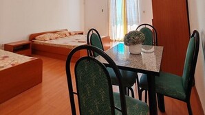 Una habitación compacta con una cama, una mesa de comedor con sillas, una mesita con una planta y una ventana con cortinas.
