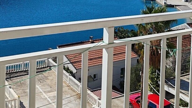 Un balcón con vista a un lago tranquilo, un muelle y un edificio con tejados rojos.