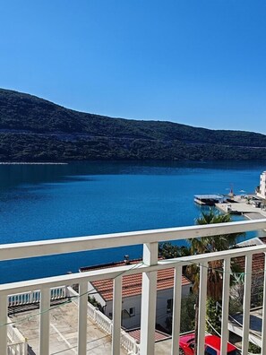 Ein Balkon mit Blick auf einen stillen See, eine Anlegestelle und ein Gebäude mit roten Ziegeldächern.