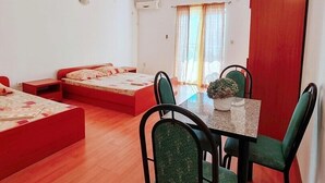 Habitación compacta con una mesa de comedor, cuatro sillas, una pequeña planta en maceta y dos camas con ropa de cama roja.