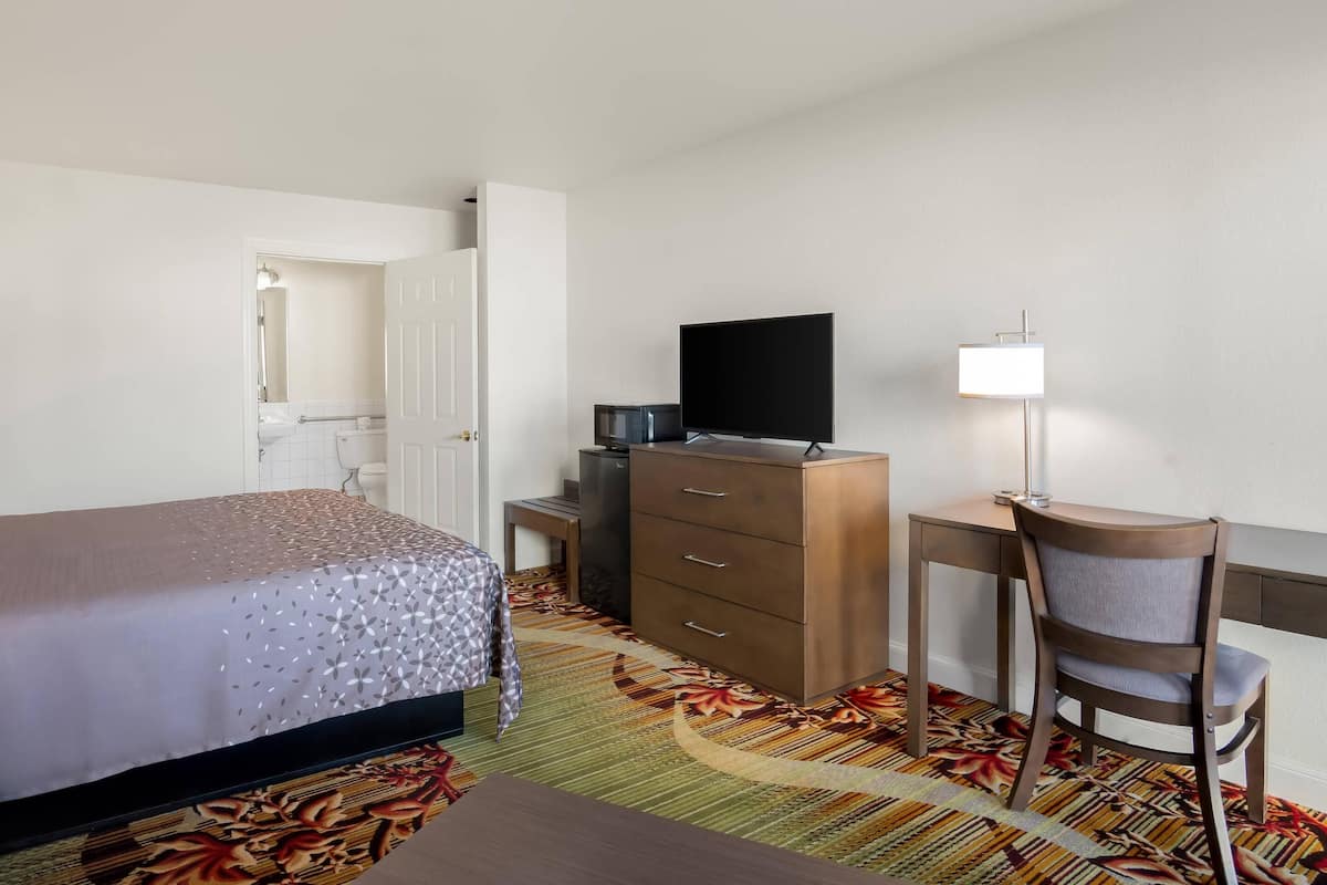 Hotellihuone, jossa on sänky, työpöytä, televisio, tuoli, lipasto ja kuviollinen matto.