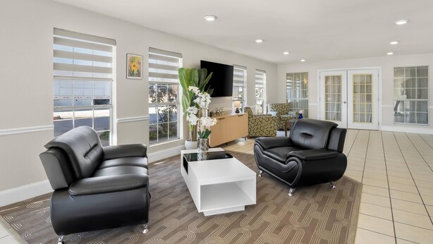 A spacious living area with two black leather sofas, a white coffee table, and a large window with blinds. - Rodeway Inn Garland Harbor Point (Garland)