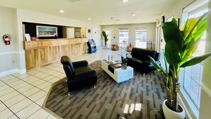 A reception area with a wooden counter, black leather chairs, a coffee table, and a large potted plant. - Rodeway Inn Garland Harbor Point (Garland)