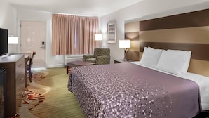 A hotel room with a bed, a desk, a chair, a TV, and a window with curtains. - Rodeway Inn Garland Harbor Point (Garland)