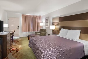 Quarto de hotel com cama, escrivaninha, cadeira, televisão e janela com cortinas.