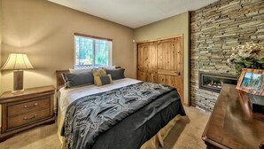 A bedroom with a bed, nightstand, dresser, stone wall, wooden door, and a fireplace.
