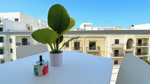 A balcony with a potted plant and a canister, overlooking a row of buildings with balconies.