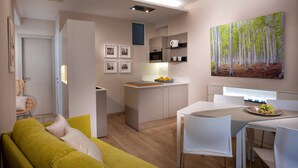 Een moderne keuken met witte kastjes, een eethoek met een witte tafel en stoelen, en een zithoek met een groene bank.