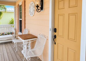 A porch with a wooden table and white wicker chairs, a decorative wall piece, and a yellow door. - 109 Georges Bay Road(Bermuda Bay) (Surfside Beach)