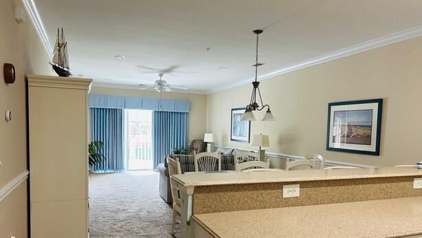 A spacious kitchen with a large island, a dining area with chairs, and a view of the outdoors through a large window. - Villa #1608 2 bedroom 2 bath (Garden City)