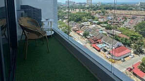 Ein Balkon mit Blick auf eine Stadtlandschaft, ein Korbstuhl und ein kleiner Tisch.