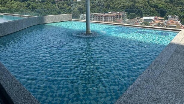 Ein Schwimmbecken mit einer zentralen Wassersp installations und Blick auf eine hügelige Landschaft im Hintergrund.