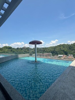 A swimming pool with a central water feature and a clear view of a hilly landscape in the background.