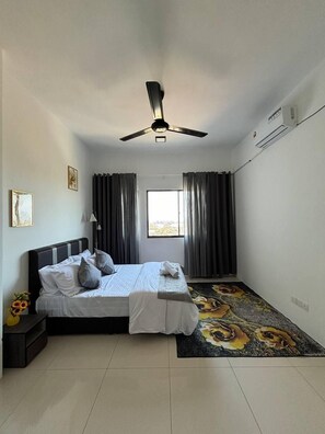 A bedroom with a bed, a ceiling fan, an air conditioning unit, a window with curtains, and a floral carpet.