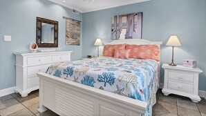 A bedroom with a bed, two nightstands, a dresser, a ceiling fan, and artwork on the walls. - Pool, Marinas & Waterfront Dining Nearby @ The Waterway 403 (Wrightsville Beach)
