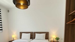 Ein Hotelzimmer mit zwei Betten, einem hölzernen Kopfteil, Nachttischlampen, einem kleinen Tisch mit Pflanze und einer Pendelleuchte.