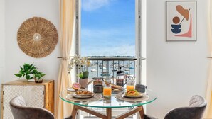Un coin repas avec une table en verre, des chaises et des aliments pour le petit-déjeuner. La fenêtre offre une vue sur les bateaux et l’eau.