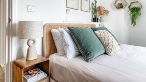 Une chambre à coucher bien rangée, avec une tête de lit en osier, une table de chevet dotée d’une lampe et un magazine posé sur la table de chevet.