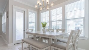 Un comedor con una mesa blanca, seis sillas y una araña.
