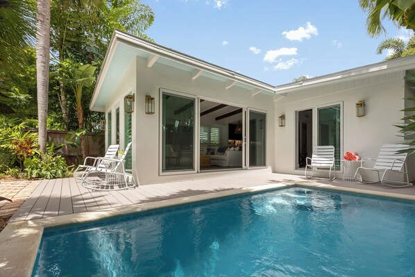 A modern house with a swimming pool, white exterior, and large sliding glass doors leading to a patio area with outdoor furniture.