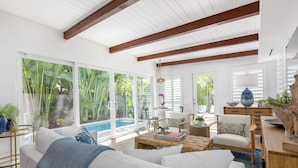 A spacious living room with a large window, a white sofa, a coffee table, and a wooden sideboard.
