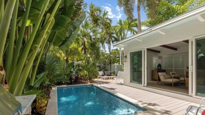 A pool with a wooden deck, surrounded by tropical plants and palm trees.