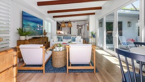 A spacious living area with a large painting, wooden beams, wicker furniture, and a view to the outside.