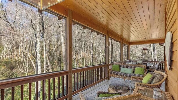Eine Holzterrasse mit Korbmöbeln und großen Fenstern mit Blick auf einen Wald.