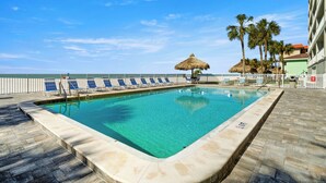 Ein Swimmingpool mit klarem, blauem Wasser, umgeben von Liegestühlen und Palmen.