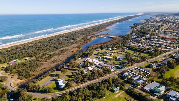 An aerial view of a coastal residential area with a beach, a river, and a mix of houses and greenery.