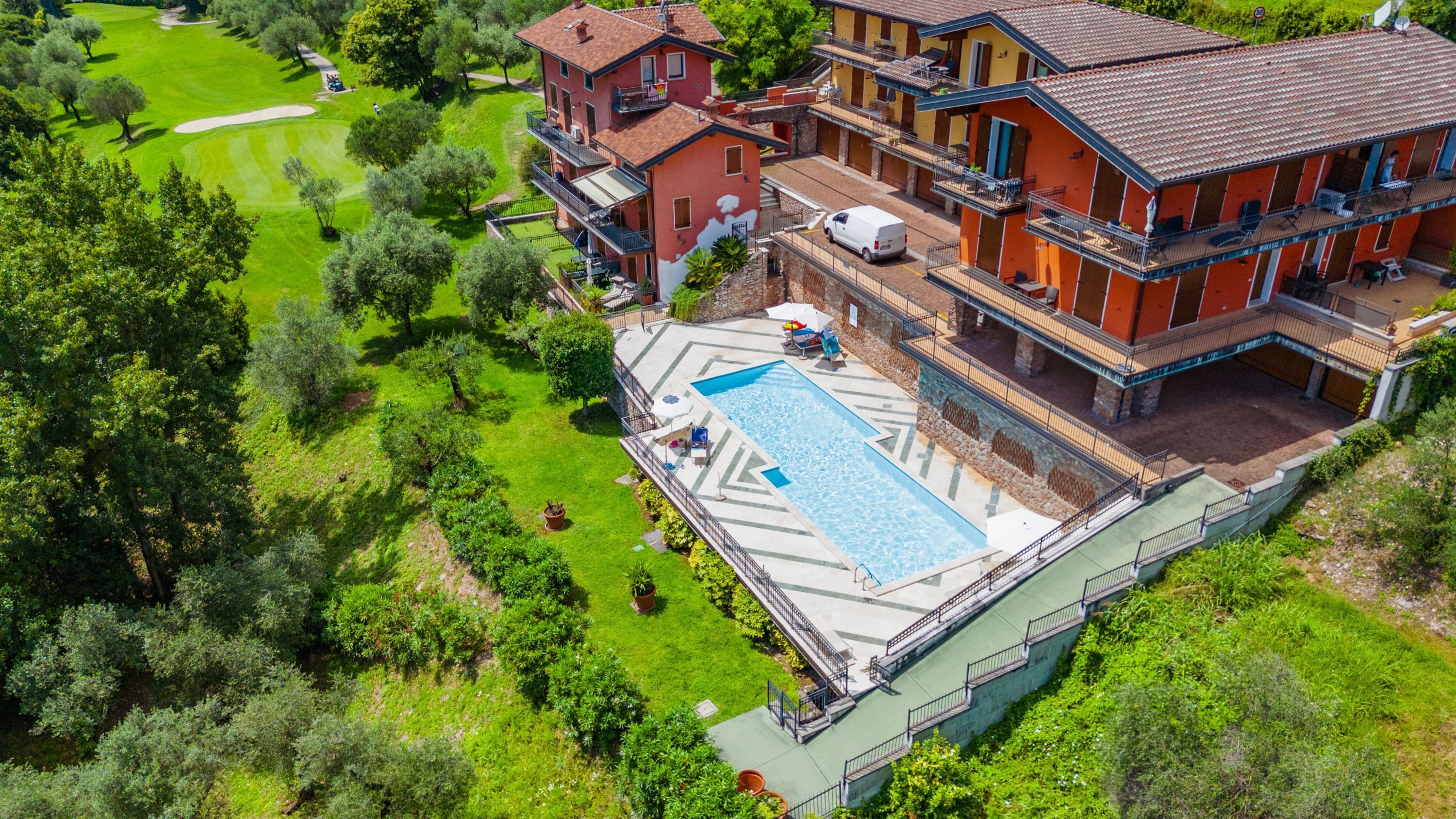 Un edificio grande con piscina, rodeado de exuberante vegetación y un campo de golf.