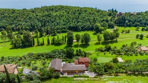 A golf course with a clubhouse, surrounded by lush greenery and a forested hill. - Residence Albatros A1 by Wonderful Italy (Toscolano Maderno)
