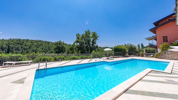 A rectangular swimming pool with clear blue water, surrounded by a tiled deck and a stone wall. - Residence Albatros A1 by Wonderful Italy (Toscolano Maderno)
