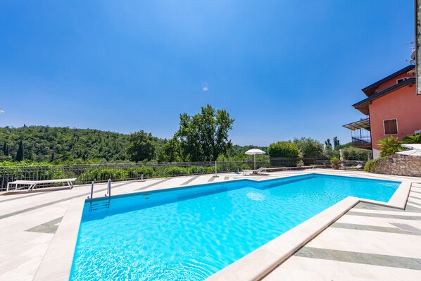 A rectangular swimming pool with clear blue water, surrounded by a tiled deck and a stone wall. - Residence Albatros A1 by Wonderful Italy (Toscolano Maderno)
