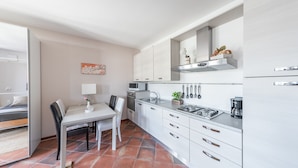 Cocina compacta con armarios blancos, una mesa de comedor con sillas, un microondas, un fregadero y una estufa.