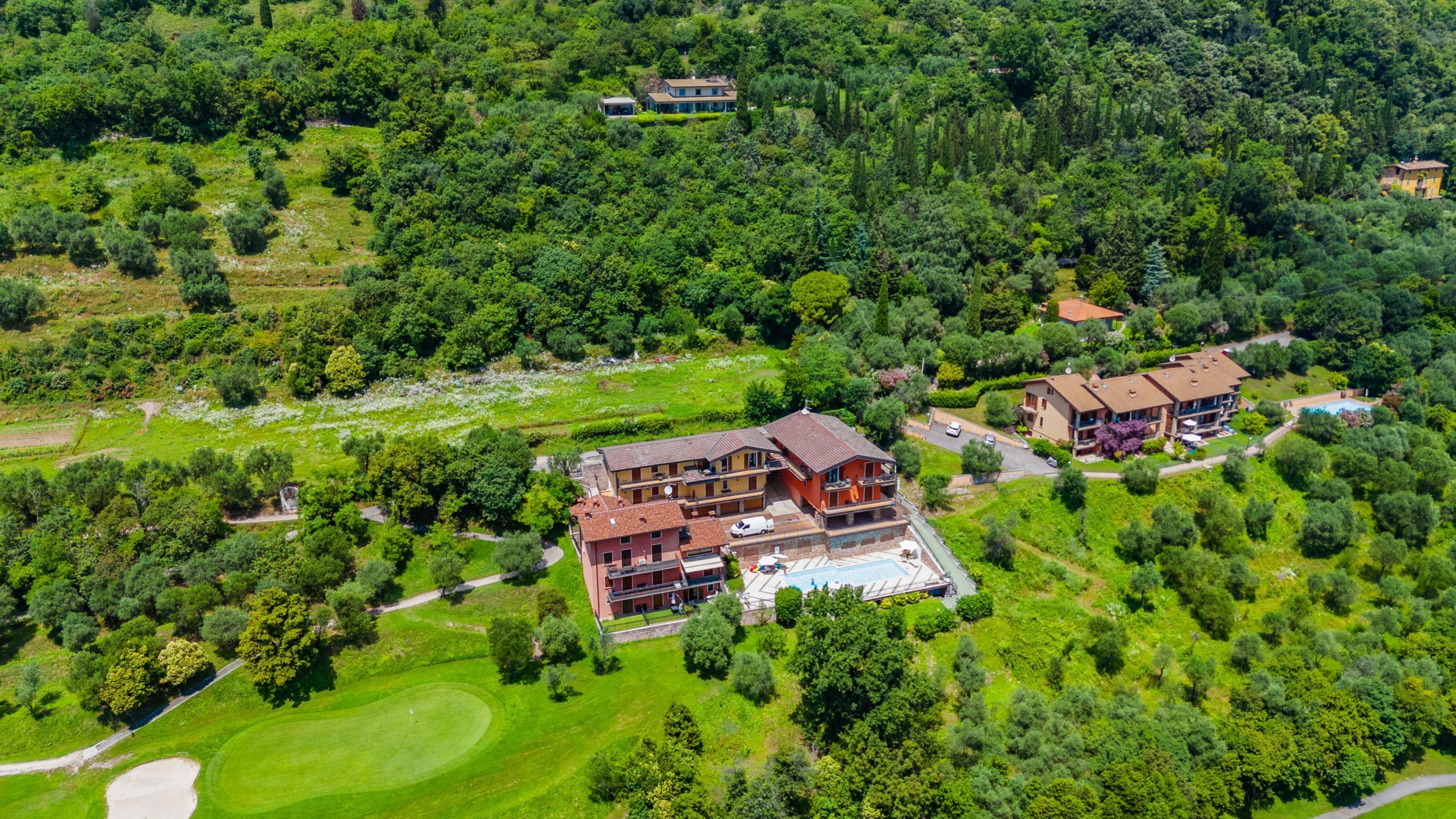 An aerial view of a large, multi-story building with a swimming pool, surrounded by lush greenery and a golf course.