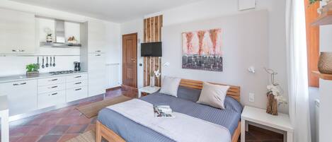 A modern bedroom with a large bed, a bedside table, a TV, and a kitchen area with cabinets and a stove.