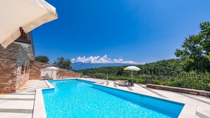 A swimming pool with a stone wall and a white umbrella, surrounded by a stone fence and greenery. - Residence Albatros A1 by Wonderful Italy (Toscolano Maderno)